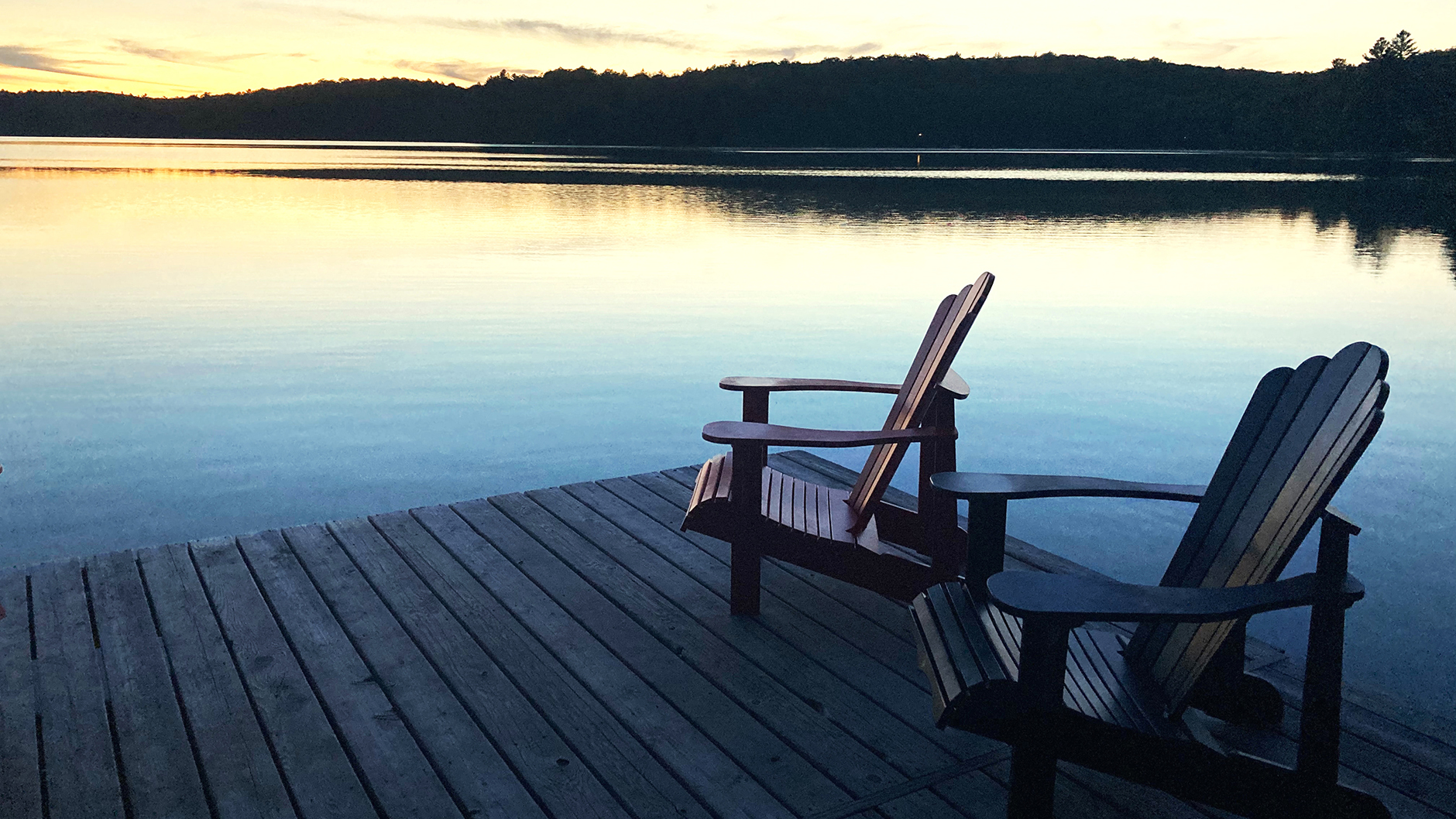 Adirondack chairs on deck beside calm lake at sunrise