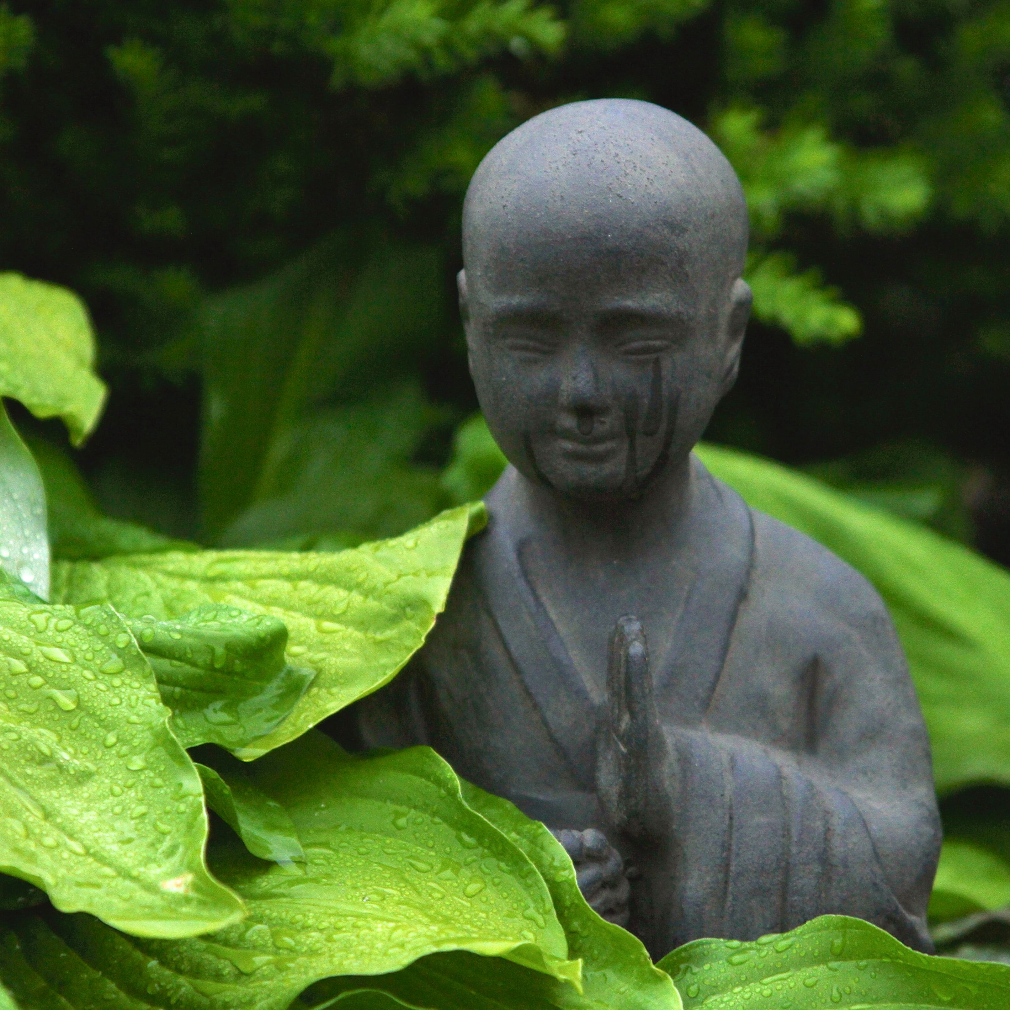 black stone statue of meditating figure amidst bright green leaves in garden