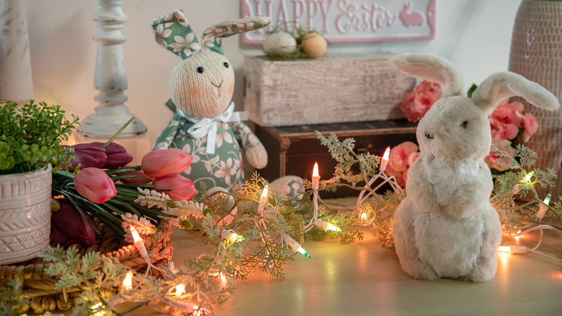tabletop Easter display featuring plush bunnies, artificial greenery and flowers and lighted pastel colored string lights