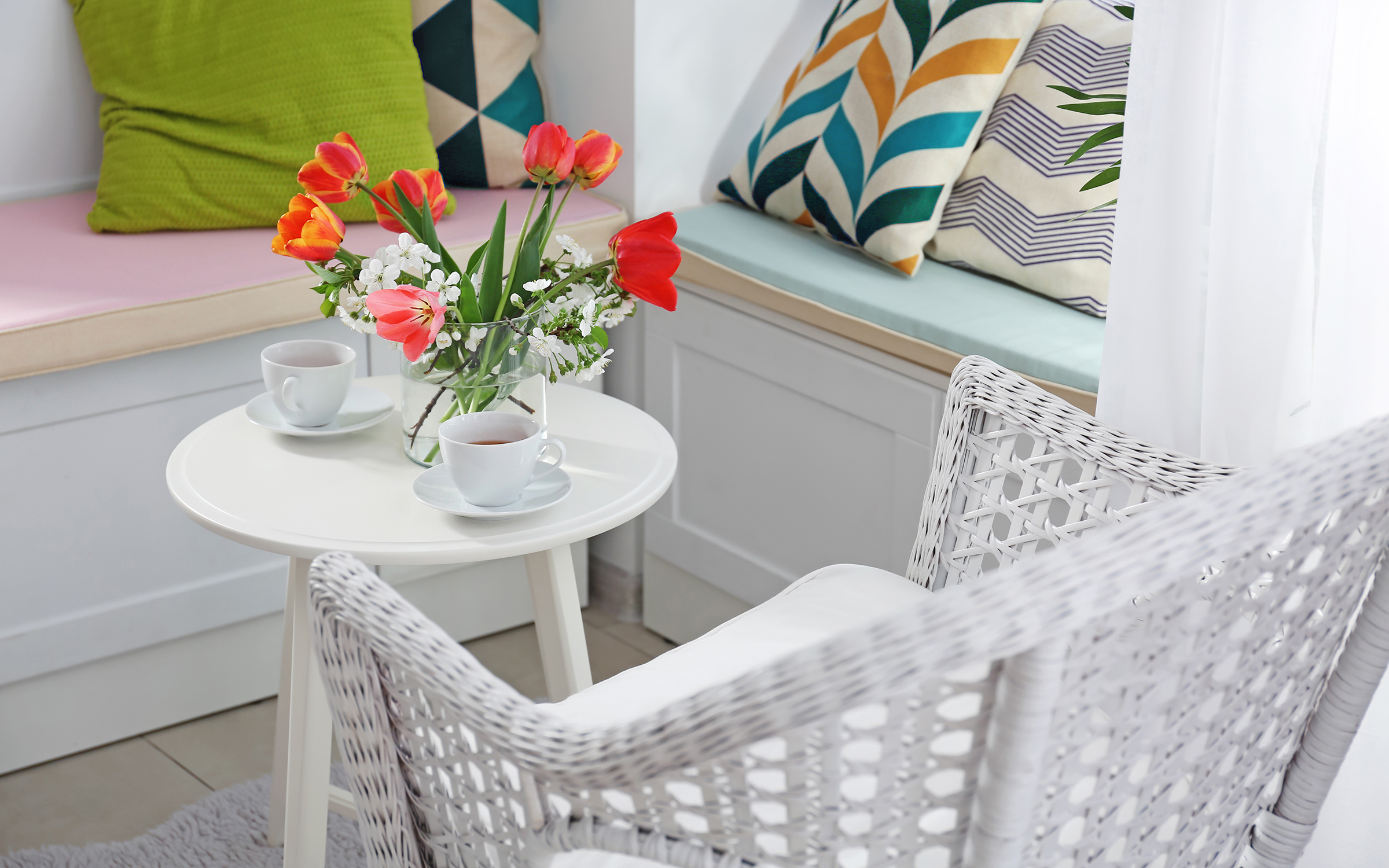 wicker porch chair, benches with colorful pillows, white table with colorful bouquet of tulips