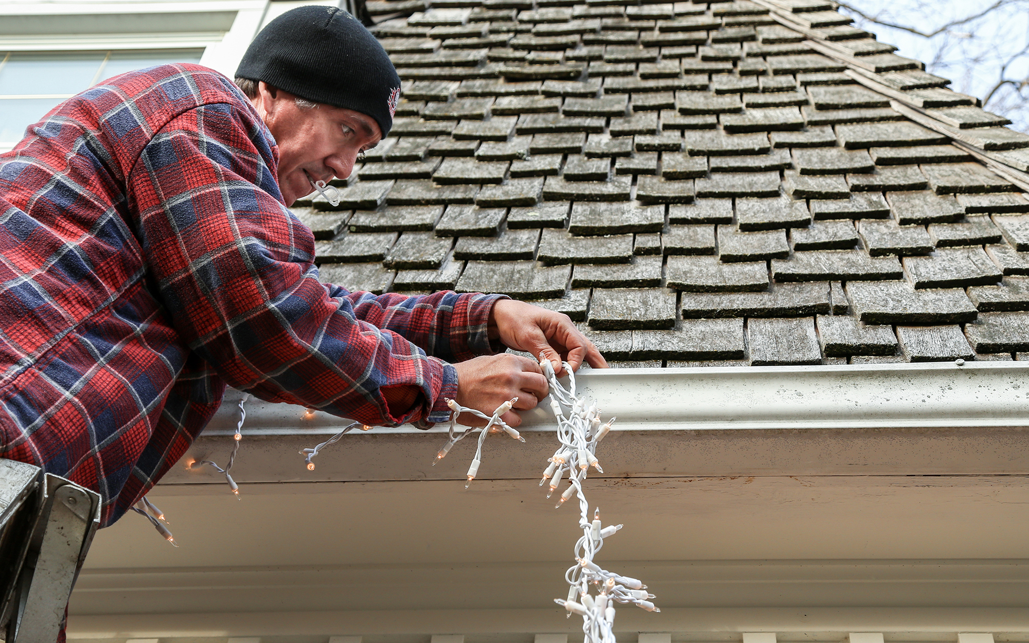man using plastic clips to attach Christmas lights to gutters