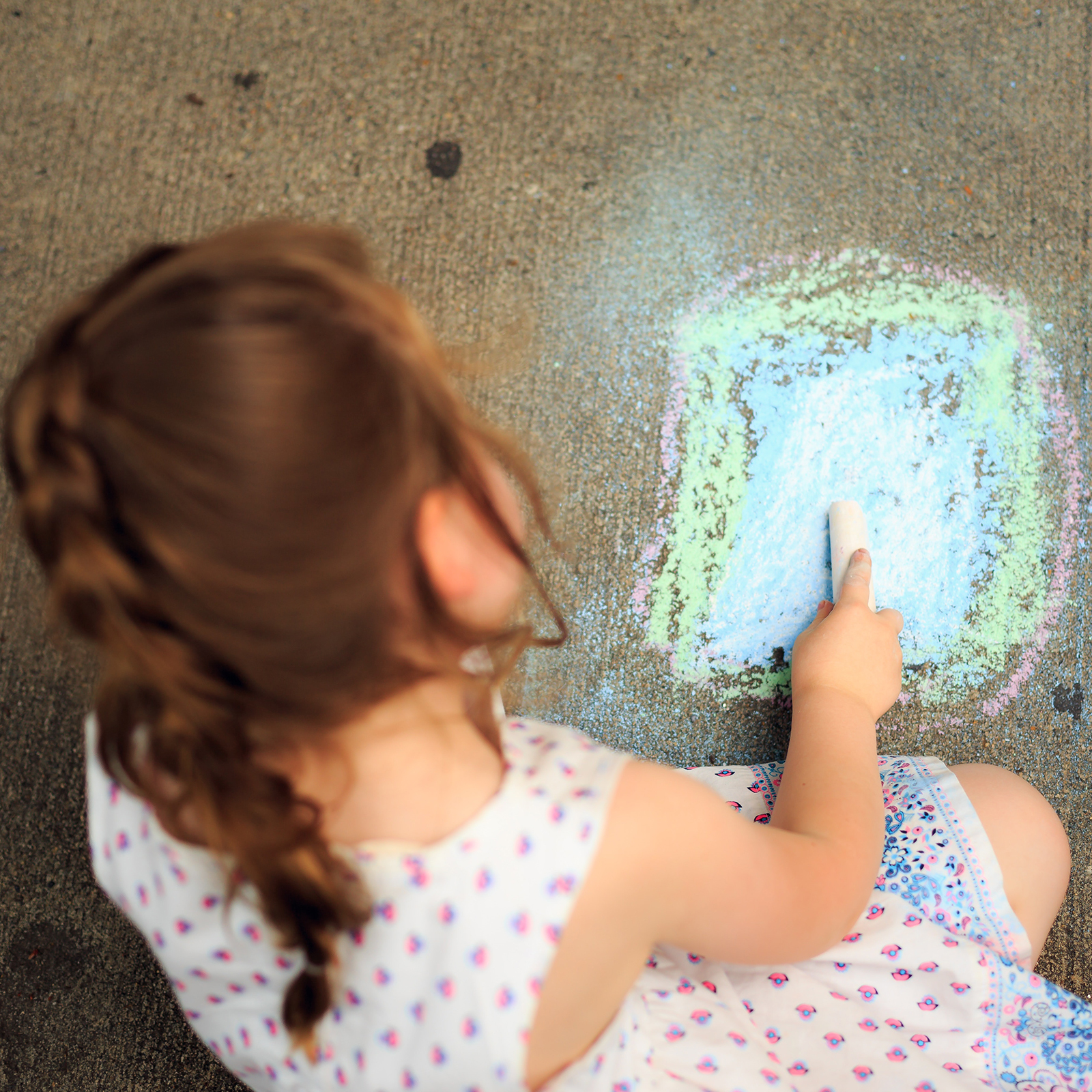 small girl drawing with chalk on pavement