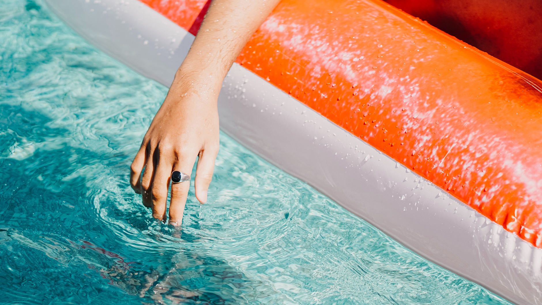 close up of hand dangling in pool water as person relaxes in an orange pool float