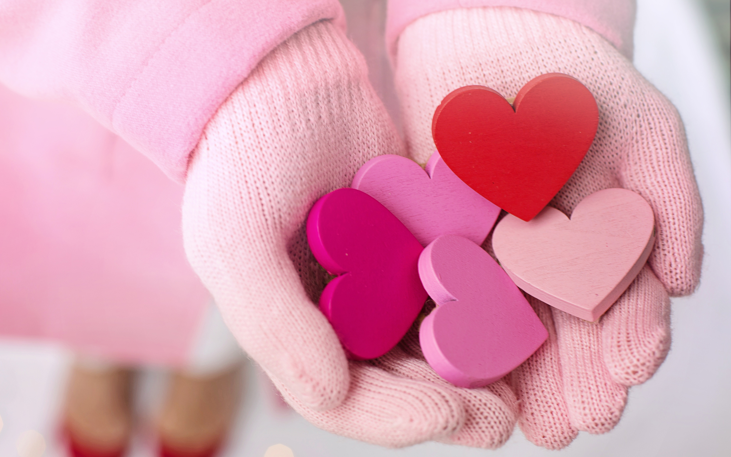pink mittened hands holding pink and red wooden hearts