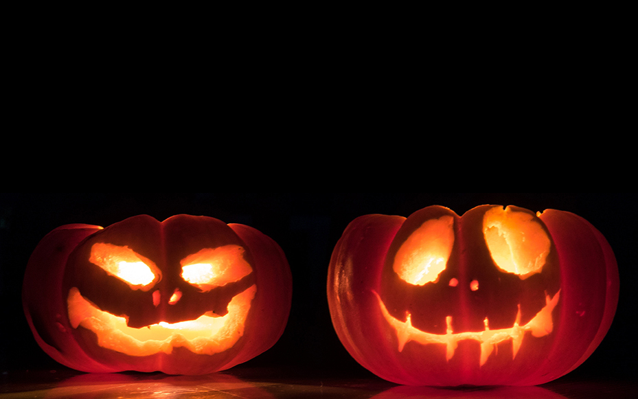 pair of spooky jack o'lantern pumpkins glow with light against a black background